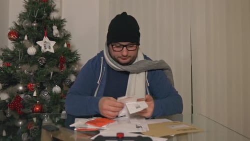 Frustrated Hopeless Man In Winter Clothes Checking Heap Of Bills To Pay During Christmas Season. dol