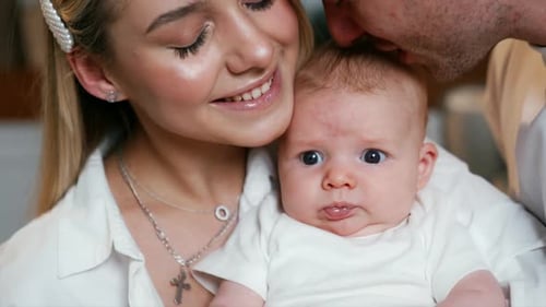 Parents hold a newborn baby kissing him on the head. Close up portrait of a happy family of three.