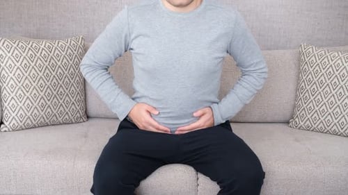 Man Rubbing Stomach in Pain Sitting on Couch