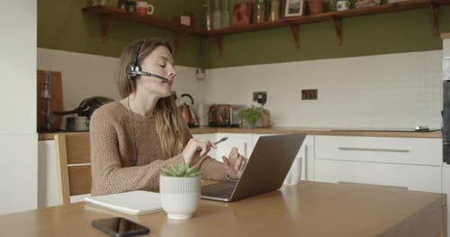 Woman with Headset Working from Home at Kitchen Table