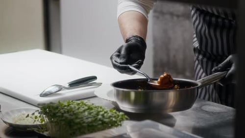Hands of Chef Serving Sauced Meat on Plate in Restaurant Kitchen