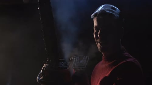 Man Holds Steaming Chainsaw Indoors in Dim Light
