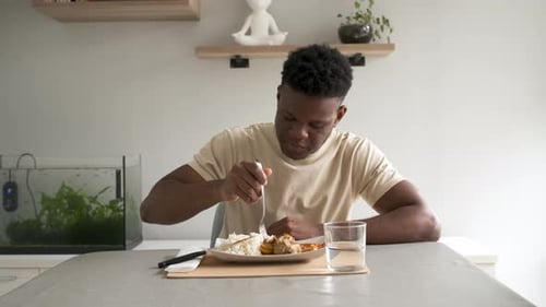Joven negro comiendo arroz con pollo frito y plátano con plato de salsa de tomate