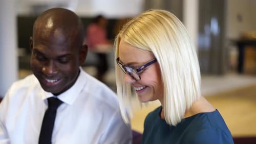 Two diverse businesspeople discuss paperwork together in modern office