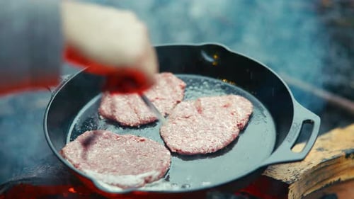 Outdoor cooking burgers on a cast iron pan over a campfire