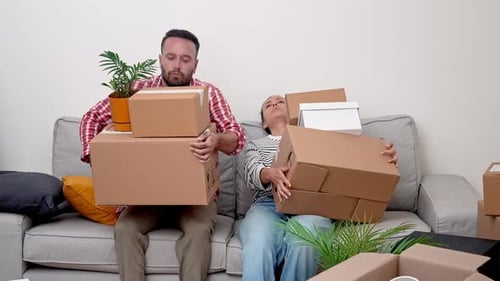 Pareja cansada al caer en un sofá con cajas de cartón agotada pero satisfecha después de mudarse a una nueva casa