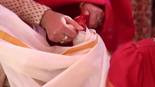 hands of a woman tying knot to clothes of bride and groom. Traditional Indian hindu wedding ritual w