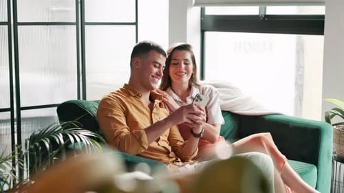 Smiling Couple Using Smartphone on Couch Indoors