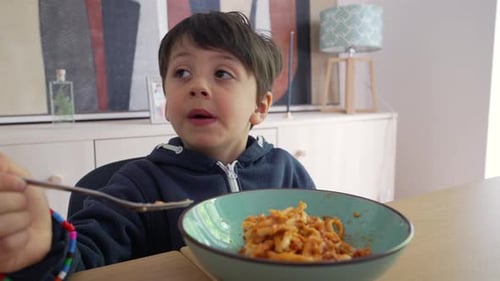 Un enfant fait tourner des spaghettis avec une fourchette, les saisissant fermement tout en se concentrant intensément sur le repas,