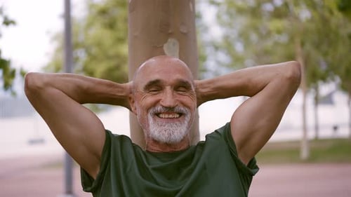 Smiling Senior Man Resting Against Tree in Park