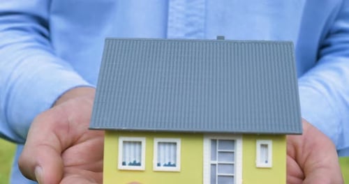 Adult Holds Miniature House in Hands