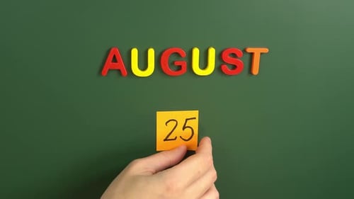 Hand sticking a sticker 25 August calendar day on school board. 25 date of august. Twenty fifth