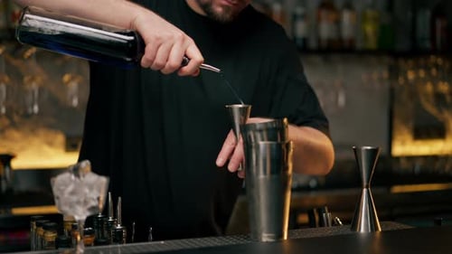 Closeup a Male Bartender Hands Holding Bottle and Masterfully Pours Liquor Into Steel Jigger