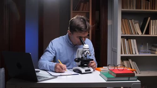 Scientist Analyzing Sample Using Microscope and Taking Notes in Laboratory
