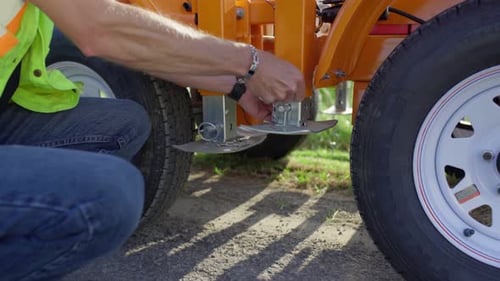 A construction worker in a yellow safety vest unlatches the metal base place of a mobile stop sign.