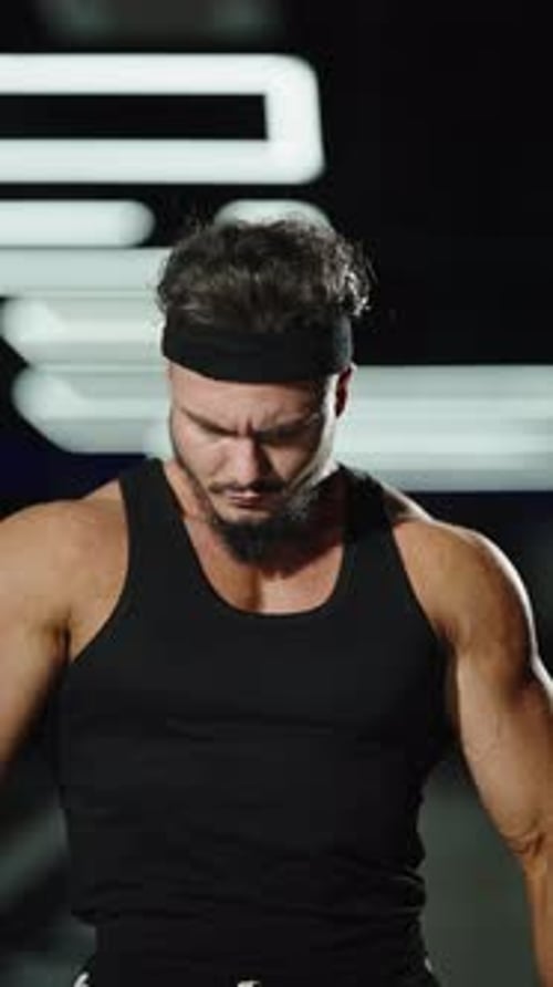 Intense Closeup of a Muscular Athlete in a Black Tank Top and Headband Under Gym Lights Shifting