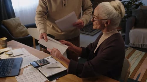 Senhora caucasiana sênior abrindo envelope com fatura não paga em atraso