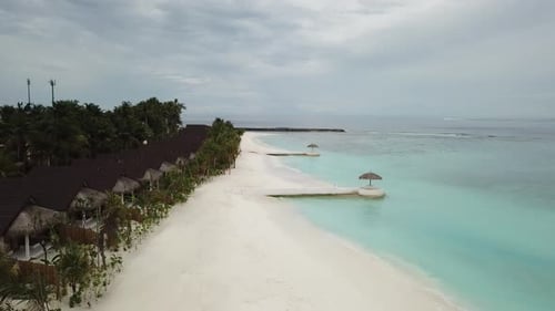 O
Drone voa acima da costa do mar em um resort nas Maldivas com vilas, palmeiras e um pássaro perto do mar.
Azul