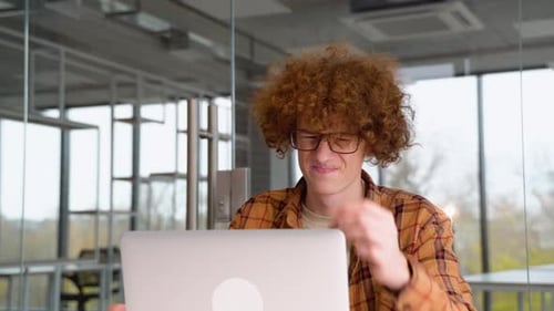 Tired Disappointed Programmer Sitting at a Table in Office and Working on a Laptop Wears Yellow