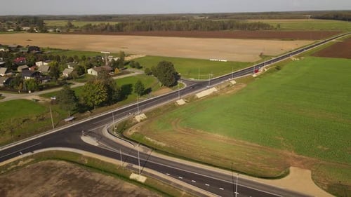 Luftaufnahme einer langen, geraden Straße, die auf einer Seite durch leuchtend grüne und goldene Felder führt und