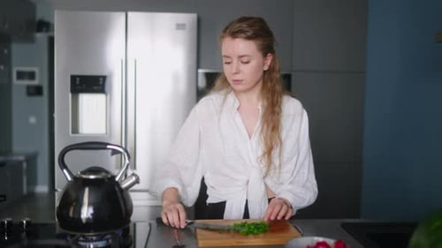 Caucasian Woman Making a Salad of Vegetables and Tasting a Meal on a Stove on Modern Kitchen Island