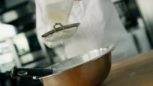 chef is sifting flour to the cooking bowl in a professional kitchen making pancakes in a restaurant