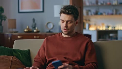 Disappointed Freelancer Reading Smartphone Message on Apartment Sofa Close Up