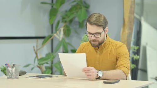 Man Reviews Documents at Desk in Office