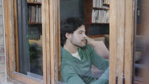 Happy caucasian man using smartphone sitting by window at home, slow motion