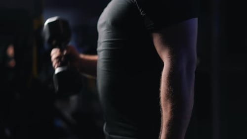 Entrenamiento muscular de bíceps para hombre fuerte con mancuernas en un gimnasio oscuro