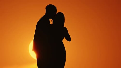 Un couple se silhouette sur un coucher de soleil avec l'homme embrassant la femme