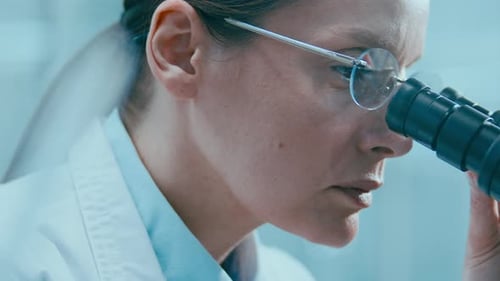 Female Scientist Looking through Microscope Eyepiece during Lab Research