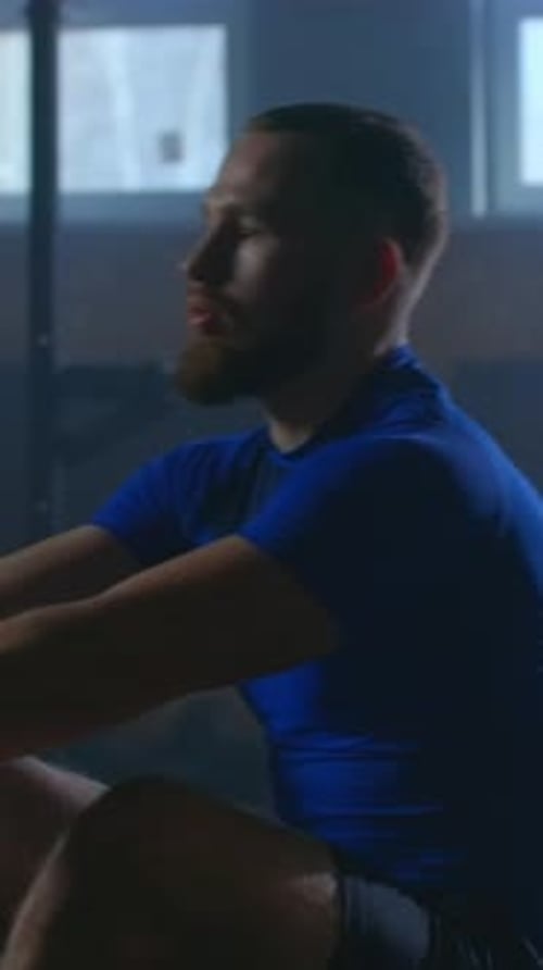 Focused Male Athlete Training on Rowing Machine in Dimly Lit Gym Transitioning From Intense Workout