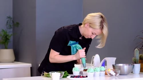 Woman Decorates Cupcakes With Green Icing in Kitchen