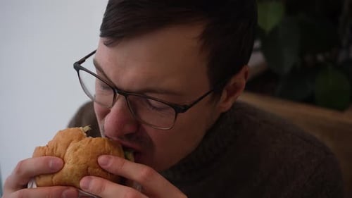 Adult enjoys hamburger and pickle indoors close up