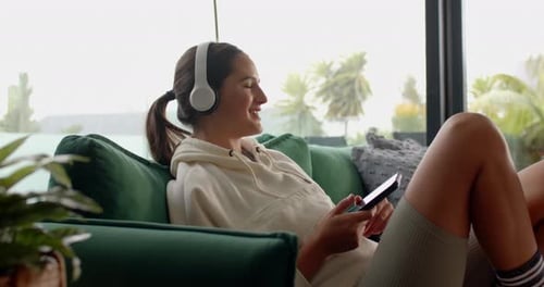 Auf der Couch entspannen, Frau mit Kopfhörern und Smartphone, Musik genießen, zu Hause