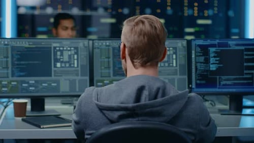 Portrait of a Smart and Handsome IT Specialist Wearing Glasses Smiles at the Camera, Behind Him Per