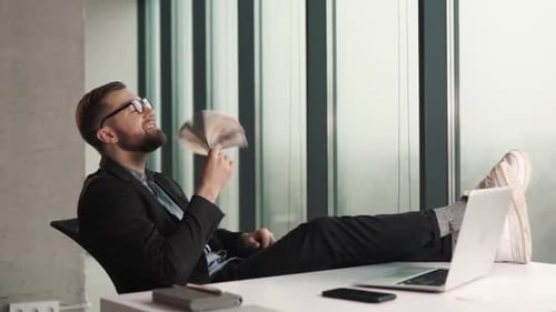 A successful man sitting at a table with a laptop waving money bills