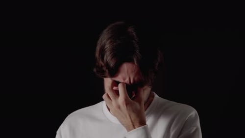 Trendiger junger Mann weint traurig, unglückliche Geste, nah, schwarzer Hintergrund