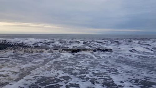 Grey muddy foaming waves crash onto a black sandy beach. ICELAND