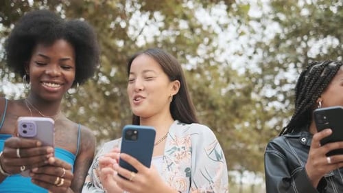 Smiling Women Friends Using Mobile Phones Outdoors