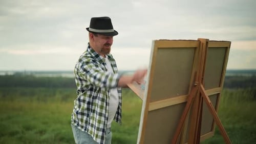 Painter in Hat and Checkered Shirt Creating Art in a Grass Field