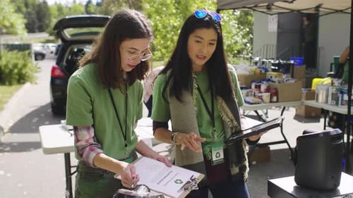 Two women sign up volunteers in green t-shirts