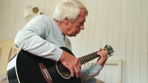 Senior Man Plays Acoustic Guitar in Bedroom