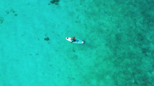 Luftbild einer Frau auf einem Surfbrett im türkisfarbenen Wasser der Malediven