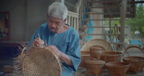 An Asian male farmer who is an elderly native basketry artisan weave basket from bamboo