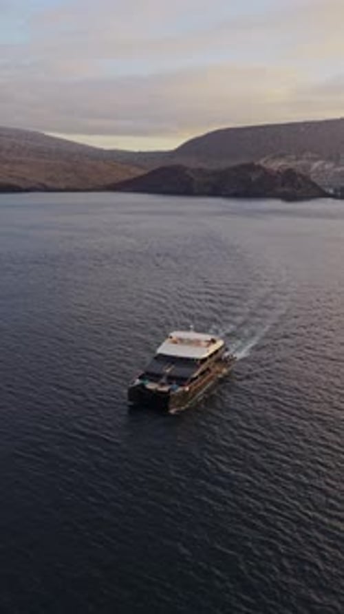 Vidéo aérienne verticale d'un catamaran moderne naviguant sur des eaux calmes à côté de l'île volcanique des Galapagos