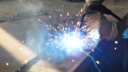 Der Schweißer auf dem Tisch schweißt eine Reihe von Metallteilen. Schweißer arbeitet. Arbeiten mit Metall