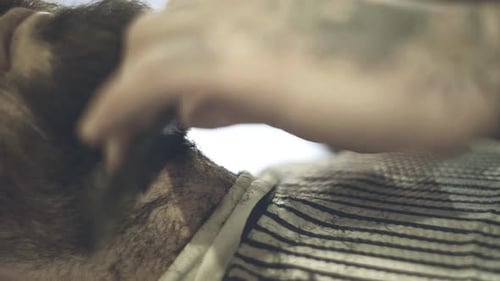 Professional barber shaves beard of male client at barbershop with razor