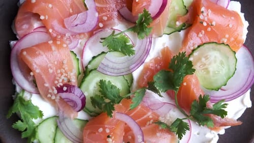 Butter board with salted salmon, cucumber, radish and cilantro on wooden plate, rotation, top view.